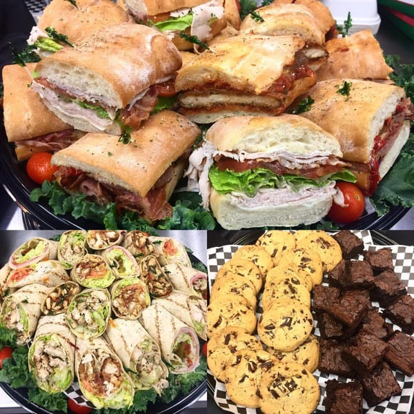 Catering trays with Italian sandwiches, wraps, chocolate chip cookies, and brownies from Marc's Pizzeria.