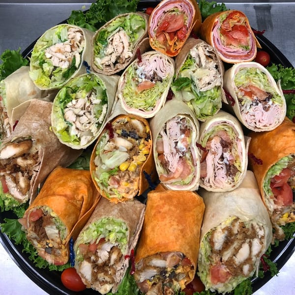 A catering platter filled with various wraps, including chicken, turkey, and ham, on a bed of lettuce.