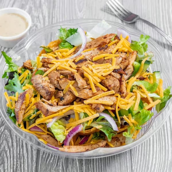 Grilled chicken salad with shredded cheddar, red onion, and lettuce in a clear bowl.