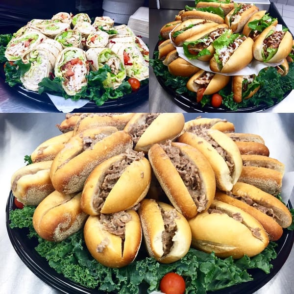 Three catering trays of Marc's Pizzeria and Grill's wraps, mini subs, and steak sandwiches.