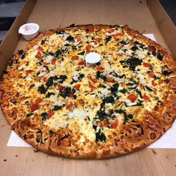 A large Marc's Pizzeria and Grill pizza with spinach, tomatoes, and cheese in a box.