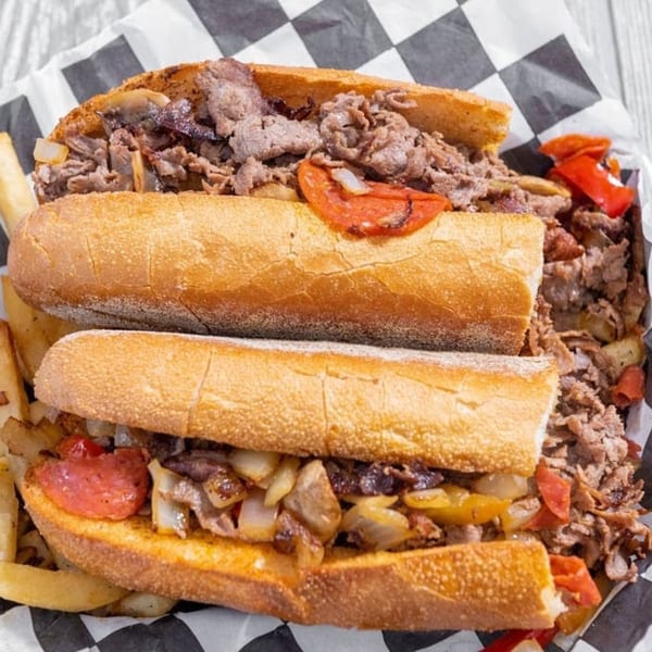 Two Marc's Pizzeria and Grill cheesesteak sandwiches with fries on checkered paper.